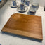 Wooden cutting board on a light gray countertop with blue and white ceramic cups in the background.